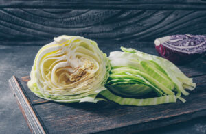 Cutting board with sliced green cabbage and a half head of purple cabbage, displayed against a textured dark background.