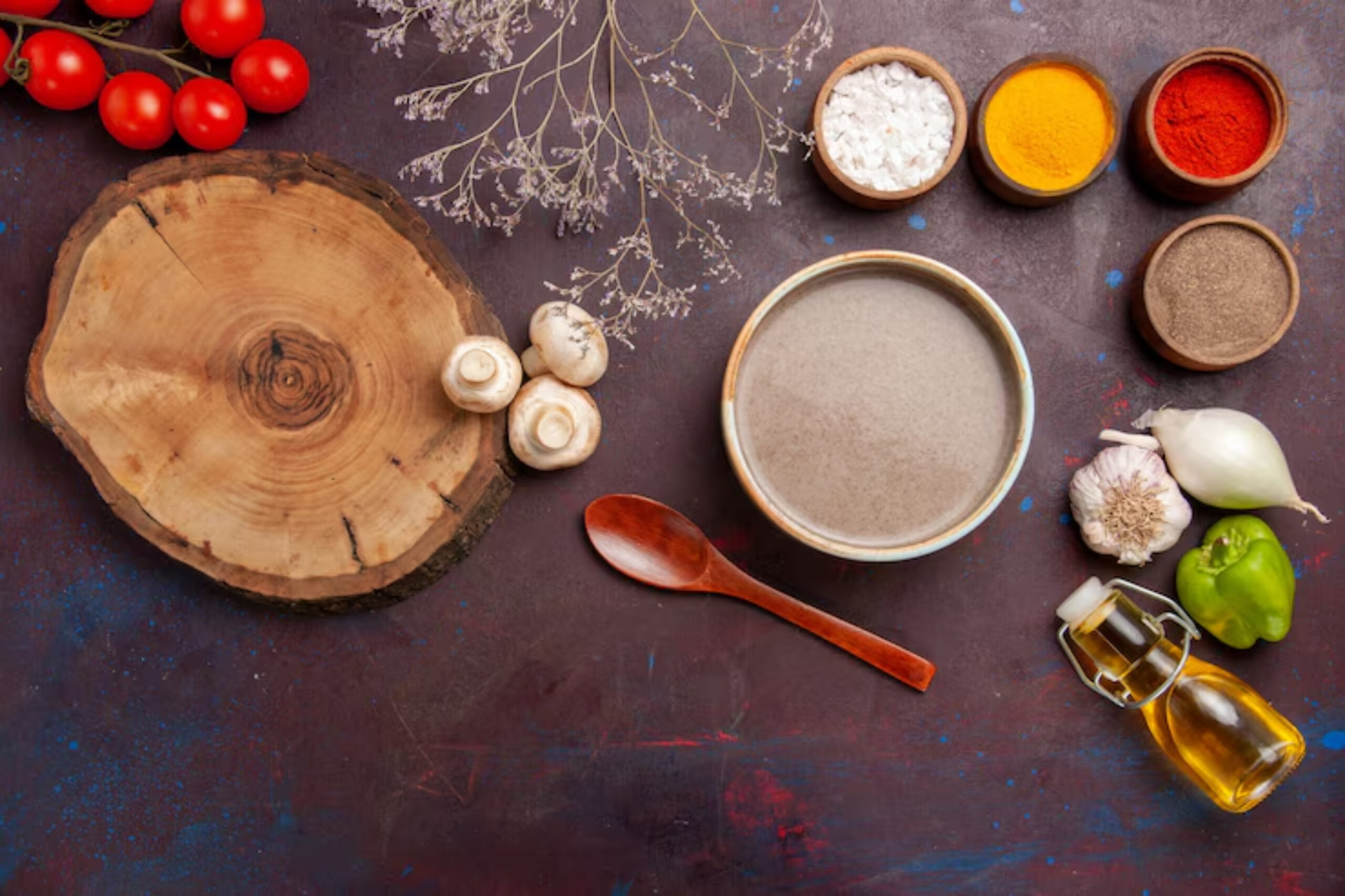Wooden board with cherry tomatoes and mushrooms on the left, next to spices and a bowl of soup on a dark surface. Ingredients include garlic, onion, and bell pepper.