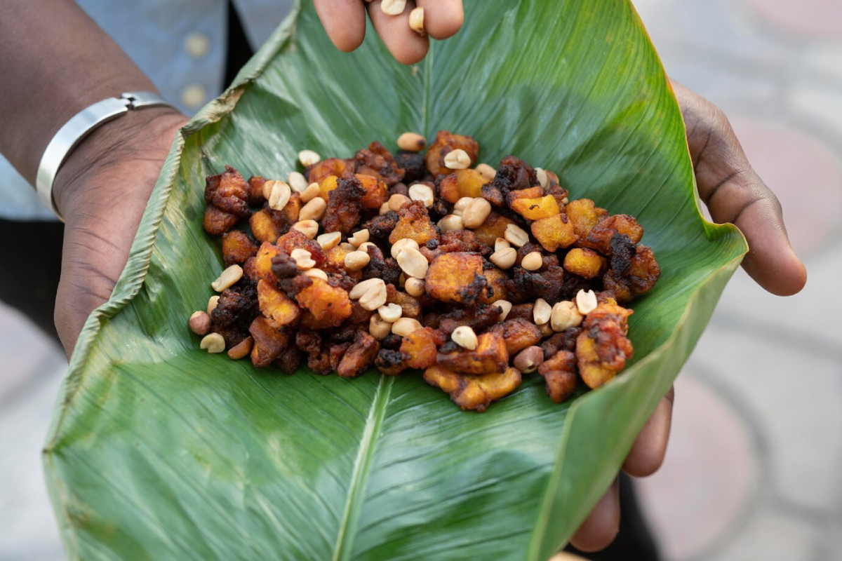 A person holds a green banana leaf filled with colorful fried plantains and peanuts, showcasing a traditional snack.
