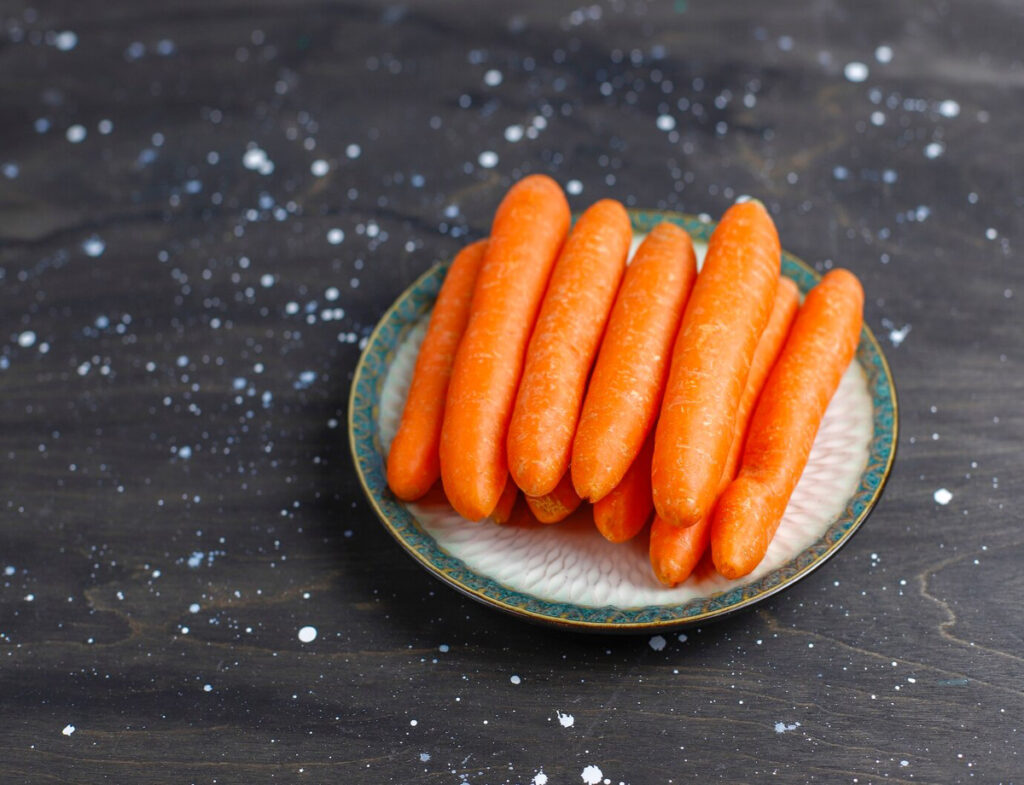 A plate of vibrant orange carrots arranged neatly on a decorative dish, set against a dark, speckled background.