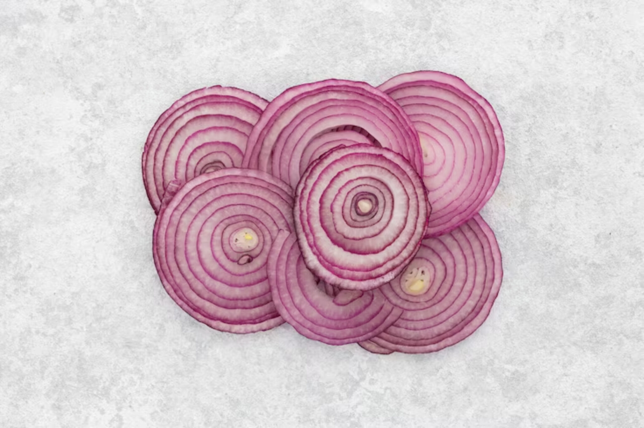 A pile of vibrant red onion slices arranged on a light textured background, showcasing their concentric rings and rich color.