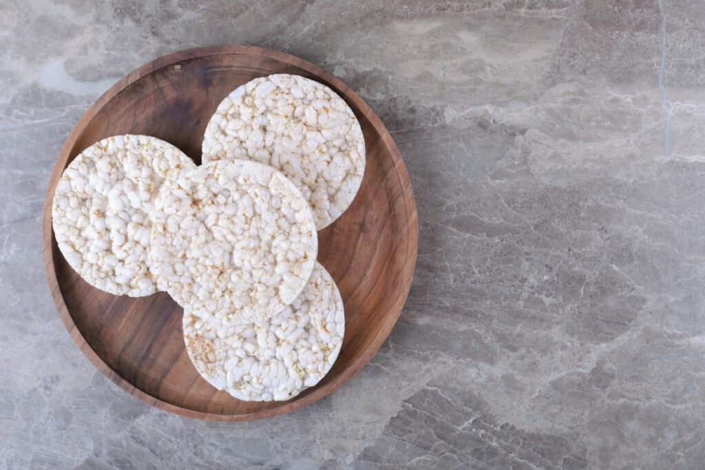 Four plain rice cakes arranged on a round wooden plate, set against a textured marble surface.
