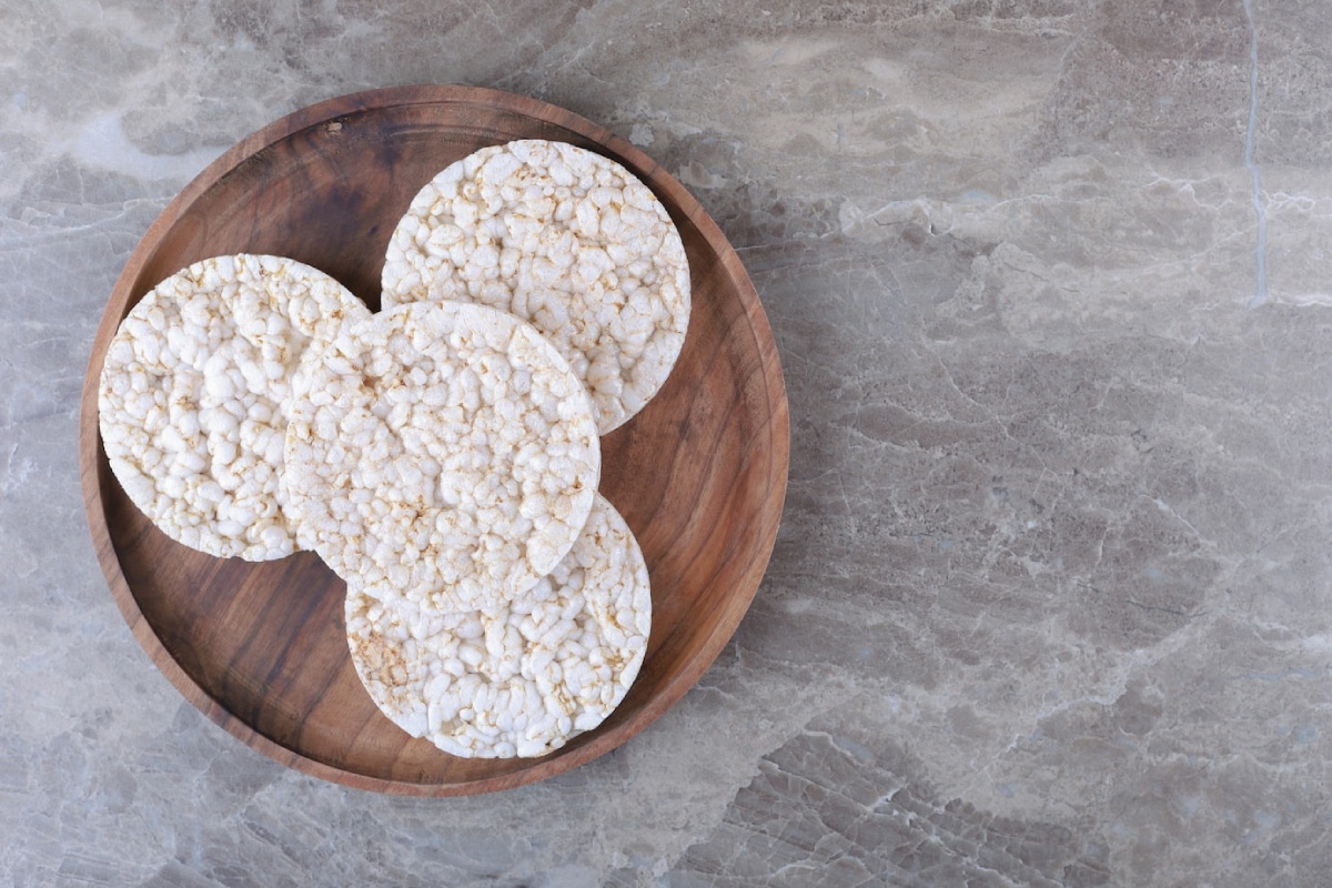 Four plain rice cakes arranged on a round wooden plate, set against a textured marble surface.