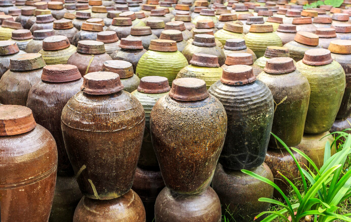 A cluster of traditional ceramic jars with textured surfaces, showcasing various earthy tones, arranged in a natural outdoor setting.